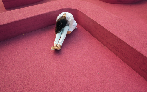 Пригнічена дівчина сидить на підлозі, обіймаючи себе | © Unsplash