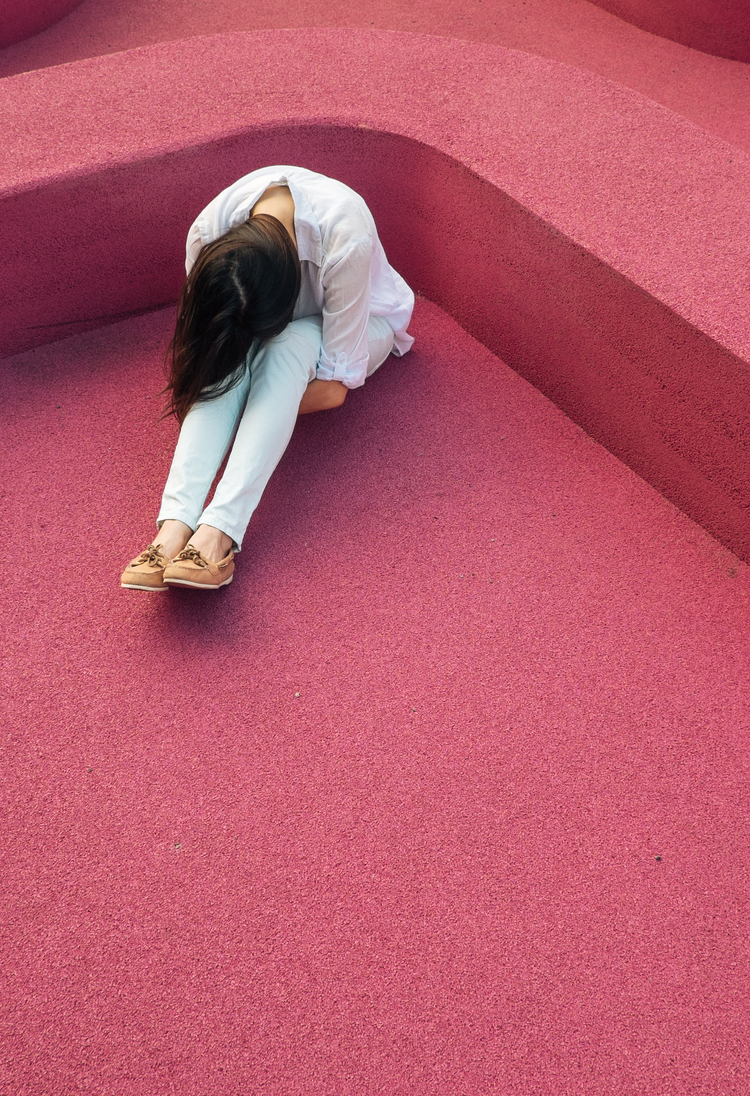 Пригнічена дівчина сидить на підлозі, обіймаючи себе | © Unsplash