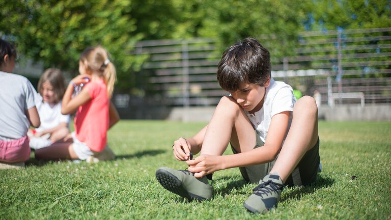 Хлопчик зав'язує взуття на газоні | © Pexels