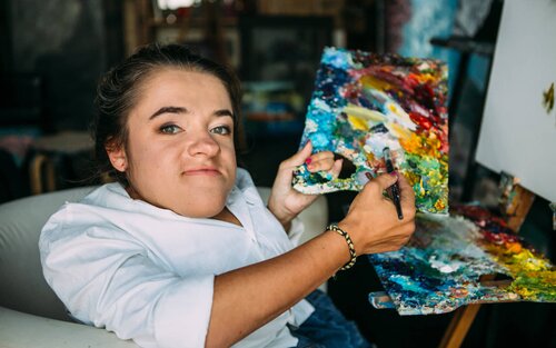 Дівчина художниця тримає палітру фарб в руках