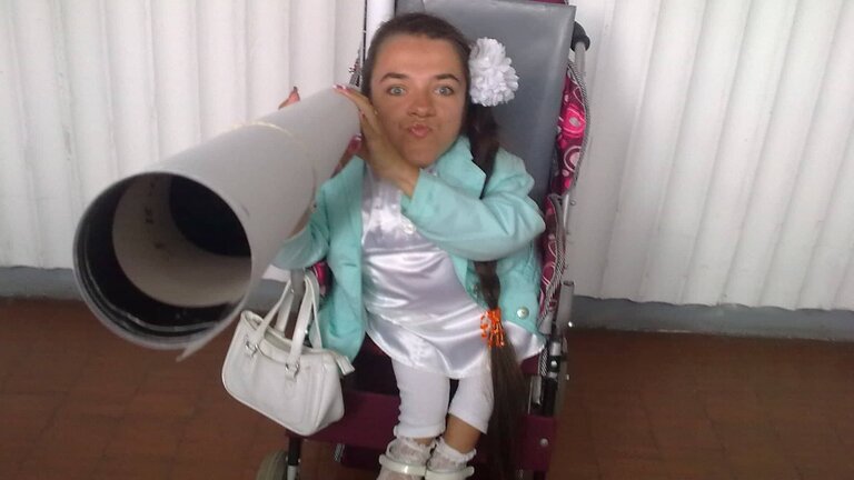 Дівчина в інвалідному візку з папером, згорнутим в трубу